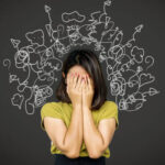 woman in green shirt covering face standing in front of a chalkboard