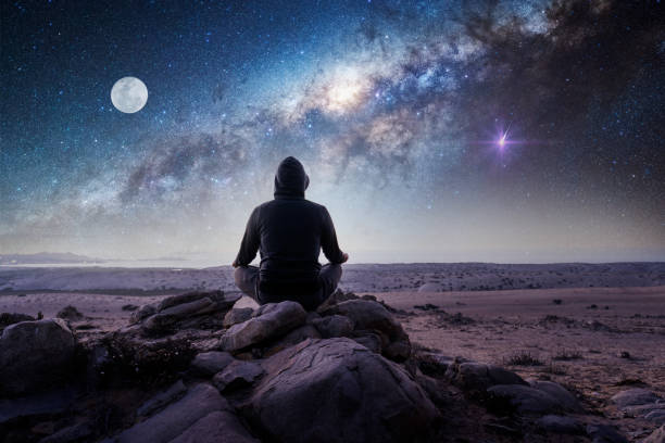 Man sitting on mountain meditating in front of the moon